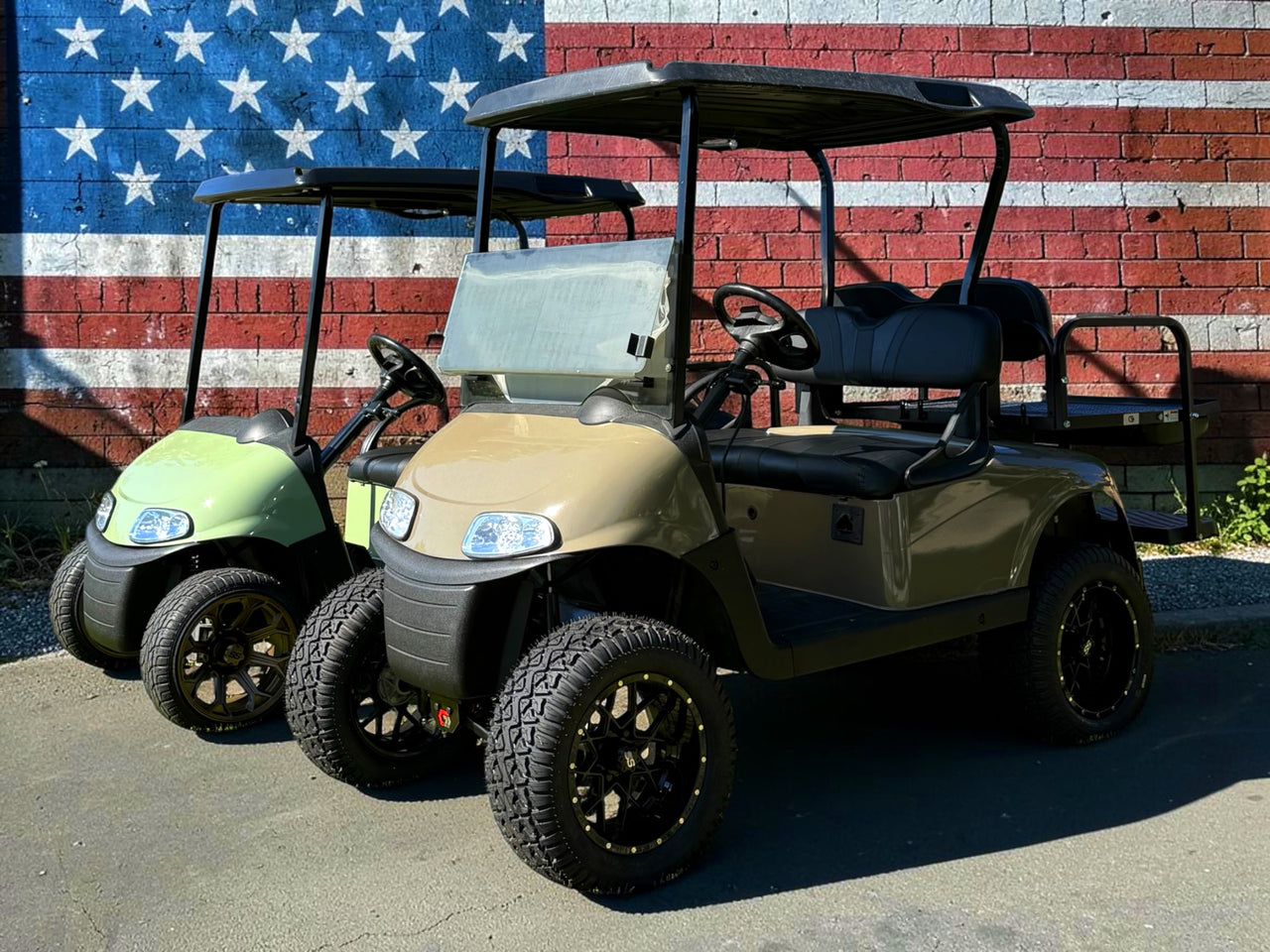 Two golf carts parked in front of a brick wall with an American flag design.